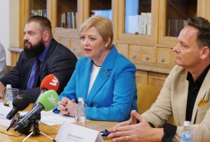 Preses konference ar trīs runātājiem pie galda, priekšplānā mikrofonu rinda