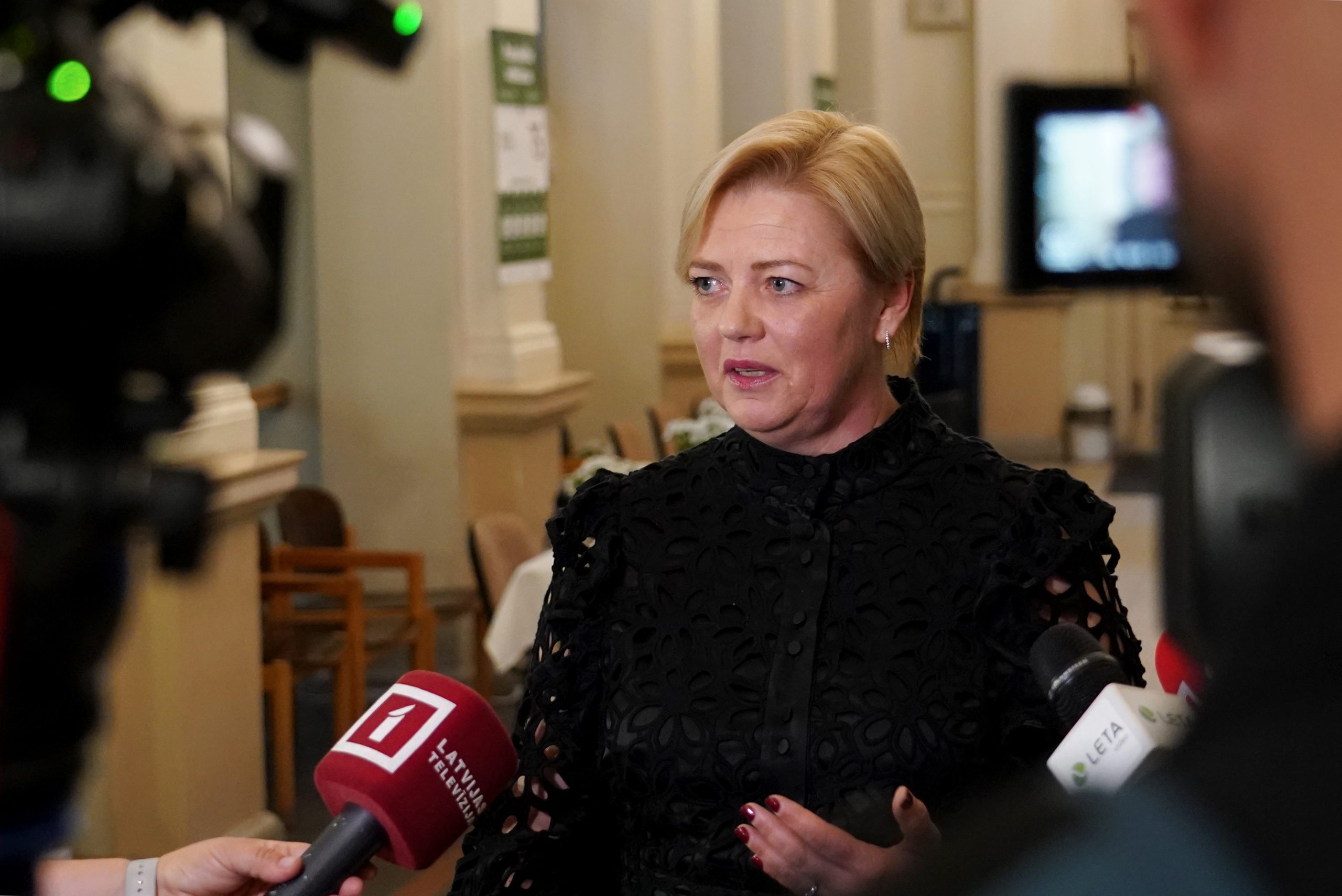 Kristīne Saulīte sniedz interviju žurnālistiem pēc komisijas sēdes, mikrofonos redzami LTV, LETA un citi logotipi.
