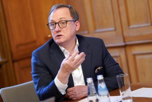 Latvijas Bankas prezidents Mārtiņš Kazāks, vīrietis brillēs uzvalkā, runā pie galda