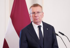 Valsts prezidents Edgars Rinkēvičs stāv pie mikrofonu statīviem Latvijas karoga priekšā