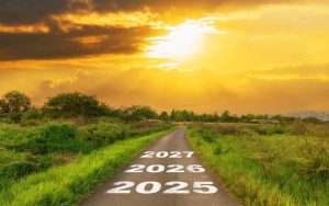 Ceļš lauku ainavā ar uzrakstiem “2025”, “2026”, “2027” ved uz horizontu saulrietā – simbolizē plānu nākotnei reto slimību jomā.