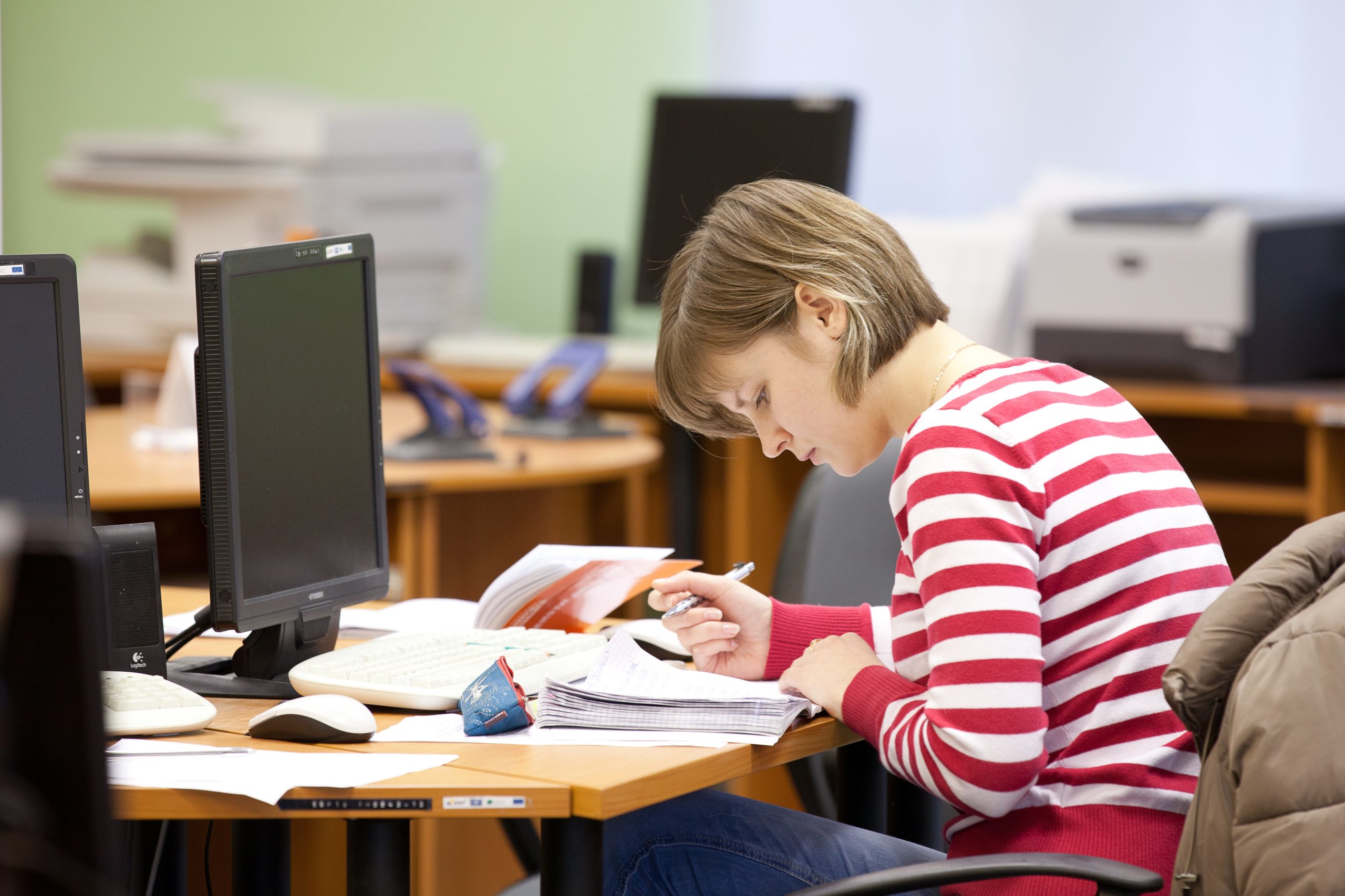 Studente sarkanbalti svītrotā džemperī mācās datoru klasē