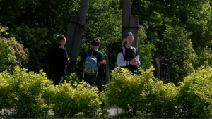 Skolēni ar mugursomām pie skolas zaļā apkārtnē