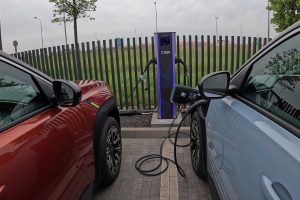 Divi elektroauto uzlādējas pie publiskās uzlādes stacijas.