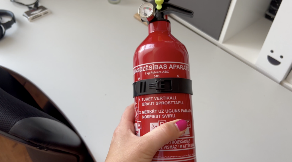 Roka tur sarkanu ugunsdzēšamo aparātu ar instrukcijām latviešu valodā
