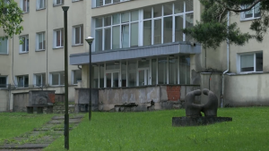 Nolietota ēkas ieeja ar betona skulptūru zālājā