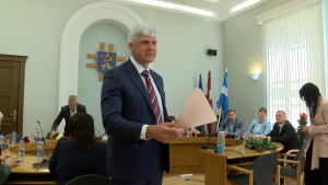 Rēzeknes domes priekšsēdētājs stāv sēdes laikā ar balsošanas kartīti rokā