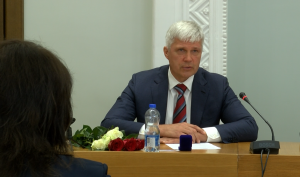 Aleksandrs Bartaševics uzrunā domes sēdē, pie galda ar rozēm un mikrofonu