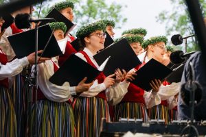 Sieviešu koris tautastērpos dzied brīvdabas koncertā ar dziesmu grāmatām rokās