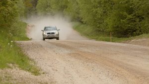 Auto brauc pa putekļainu zemes ceļu meža ieskāvumā