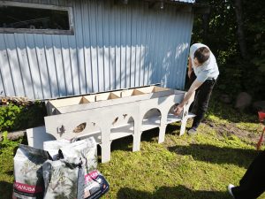 Vīrietis uzstāda kaķu mājiņu pagalmā blakus barības maisiem