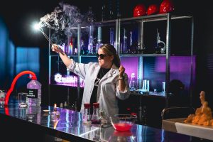 Sieviete laboratorijas halātā un saulesbrillēs veic iespaidīgu eksperimentu ar dūmiem Ventspils zinātnes centrā VIZIUM.