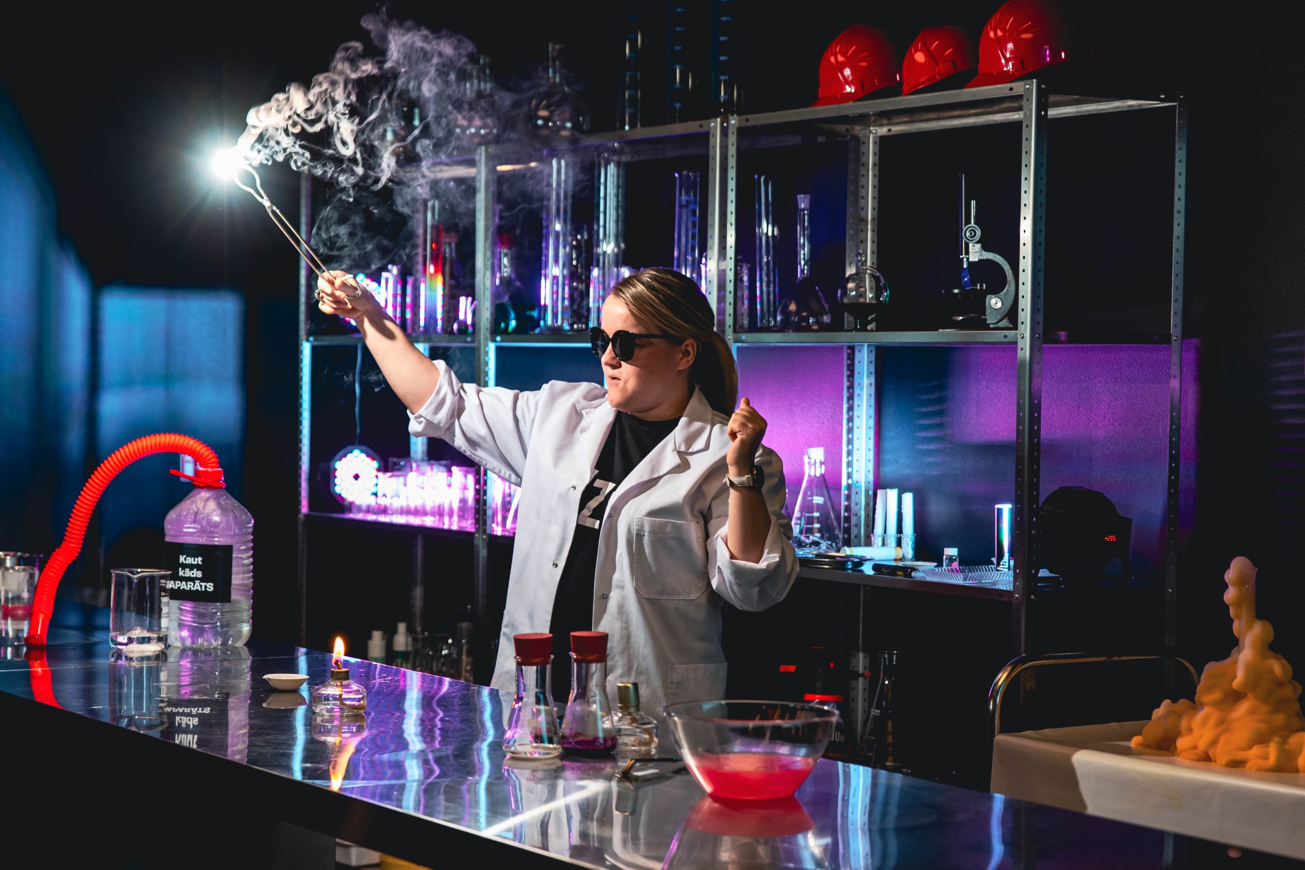 Sieviete laboratorijas halātā un saulesbrillēs veic iespaidīgu eksperimentu ar dūmiem Ventspils zinātnes centrā VIZIUM.