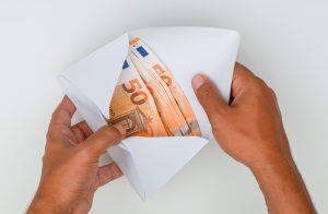 Rokas atver aploksni, kurā redzami 50 eiro banknošu saišķi.