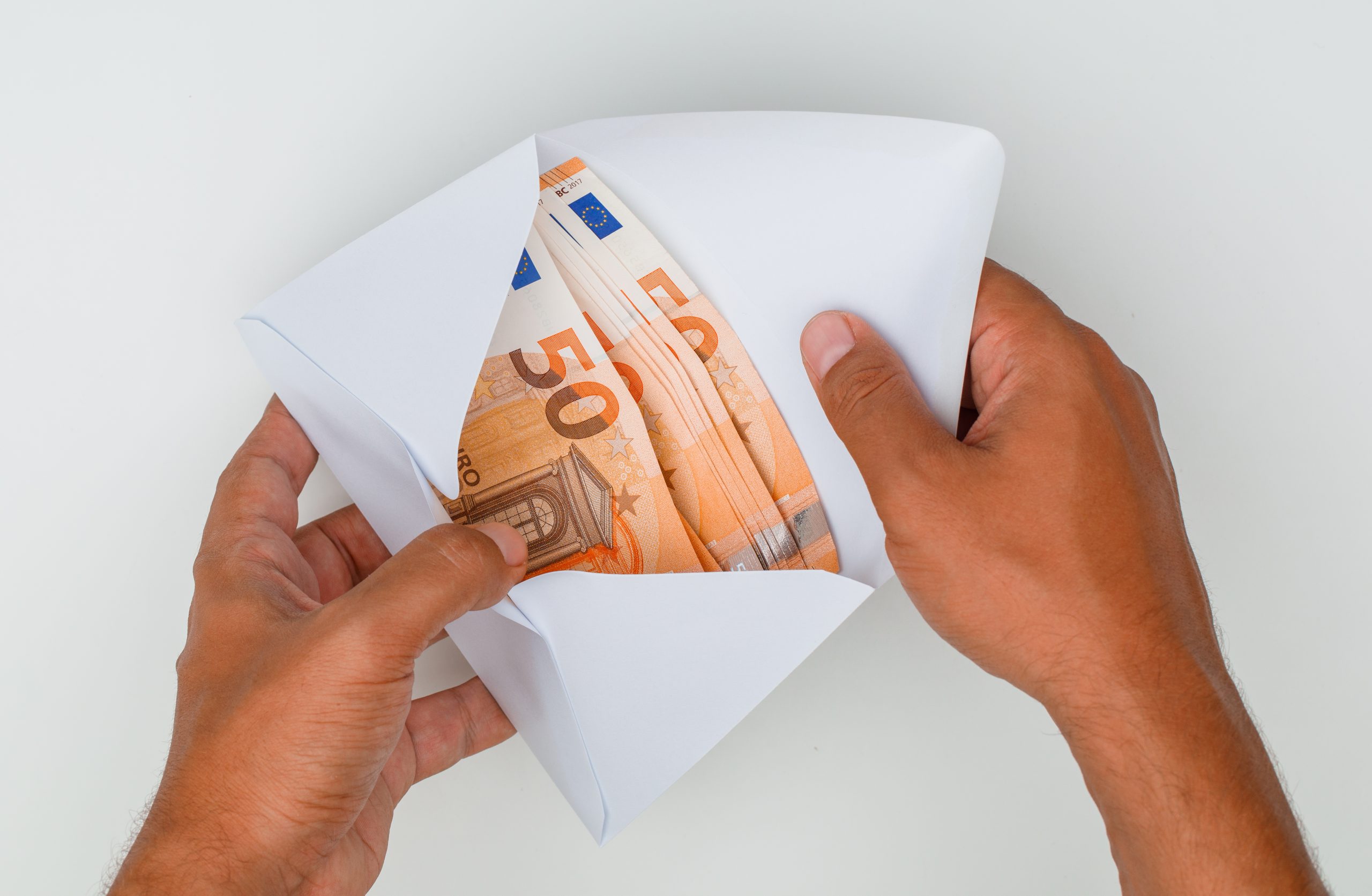Rokas atver aploksni, kurā redzami 50 eiro banknošu saišķi.