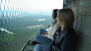 Divas sievietes sēž augstumā un skatās uz ainavu aiz drošības režģa