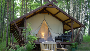 Glamping mājiņa meža vidū ar koka terasi un iedegtu lampu iekšpusē
