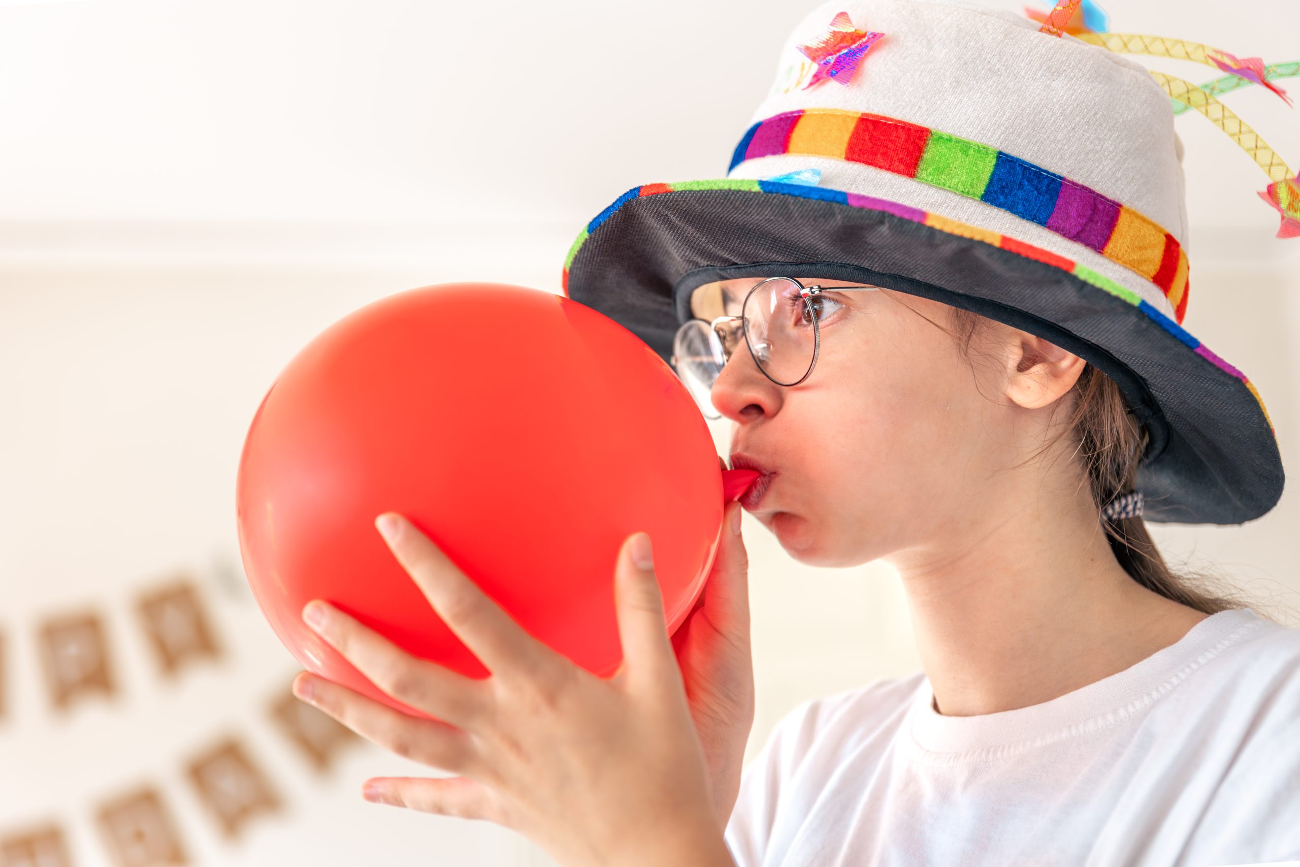 Jauna meitene krāsainā cepurē pūš sarkano balonu