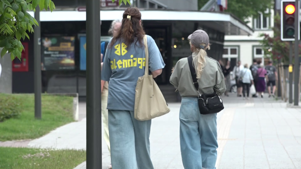 Divas personas pastaigājas pa ietvi Liepājā, redzami veikalu skatlogi fonā