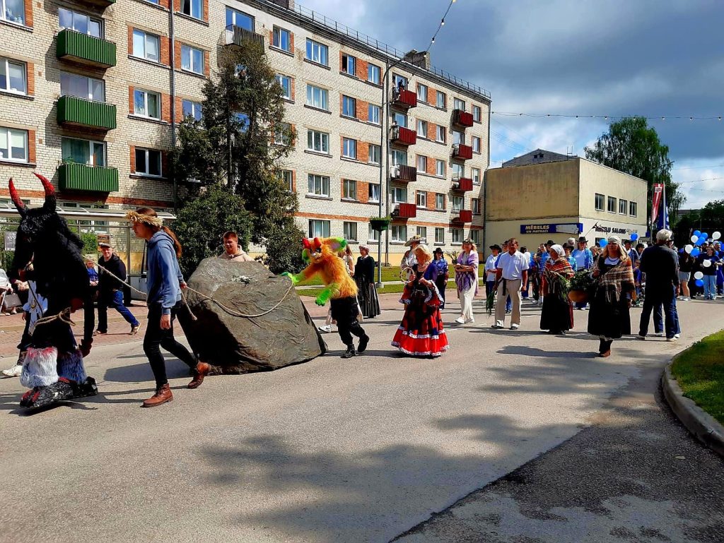 Krāsains gājiens pa ielu ar cilvēkiem dažādos kostīmos, ieskaitot "velnu", "purva mošķi" un tautas tērpus, ar ēkām fonā