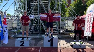 Trīs sportisti uz goda pjedestāla ar Latvijas karogu