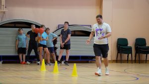 Treneris vada basketbola nodarbību bērniem Ozolnieku vidusskolas sporta projektā.