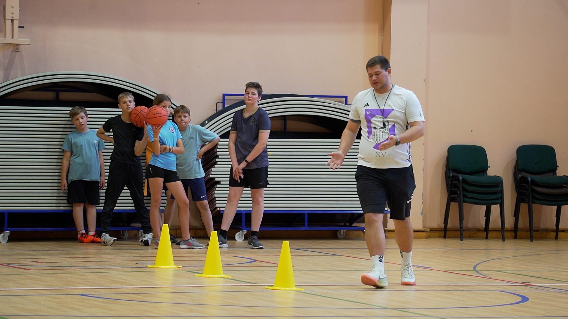 Treneris vada basketbola nodarbību bērniem Ozolnieku vidusskolas sporta projektā.