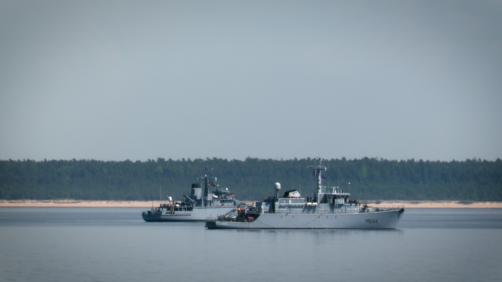 Divi militārie kuģi jūrā ar mežainu krastu fonā "BALTOPS 2025" mācību laikā