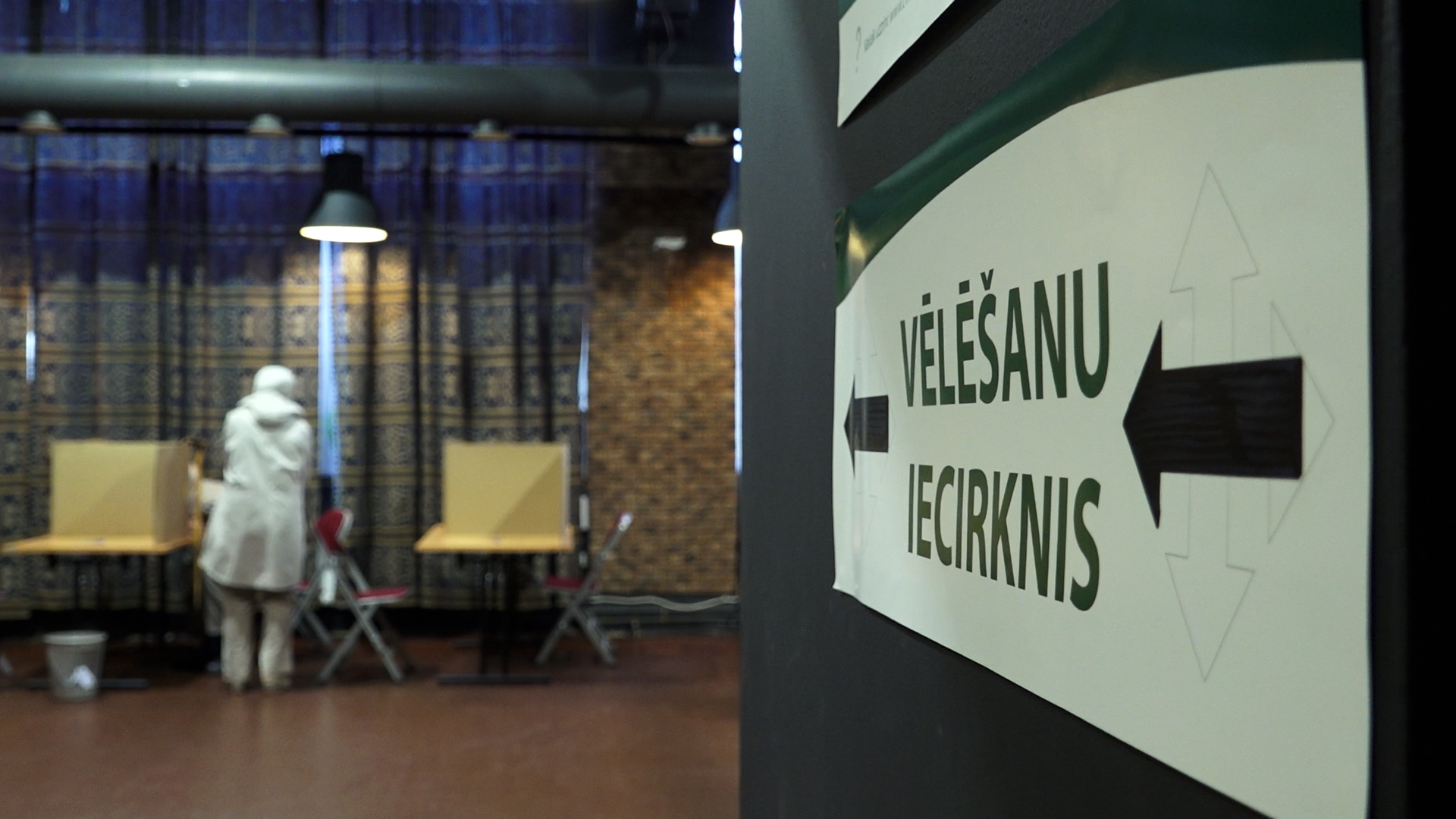 Sieviete balsošanas iecirknī pie vēlēšanu kabīnēm
