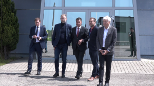 Pieci vīrieši uzvalkos pie ēkas ieejas, oficiāla vizīte vai tikšanās.