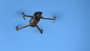 Pelēks DJI Mavic 3 drons lido skaidrās, zilās debesīs