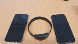 Elektroniskās uzraudzības aproce un divas rokas ierīces uz galda.