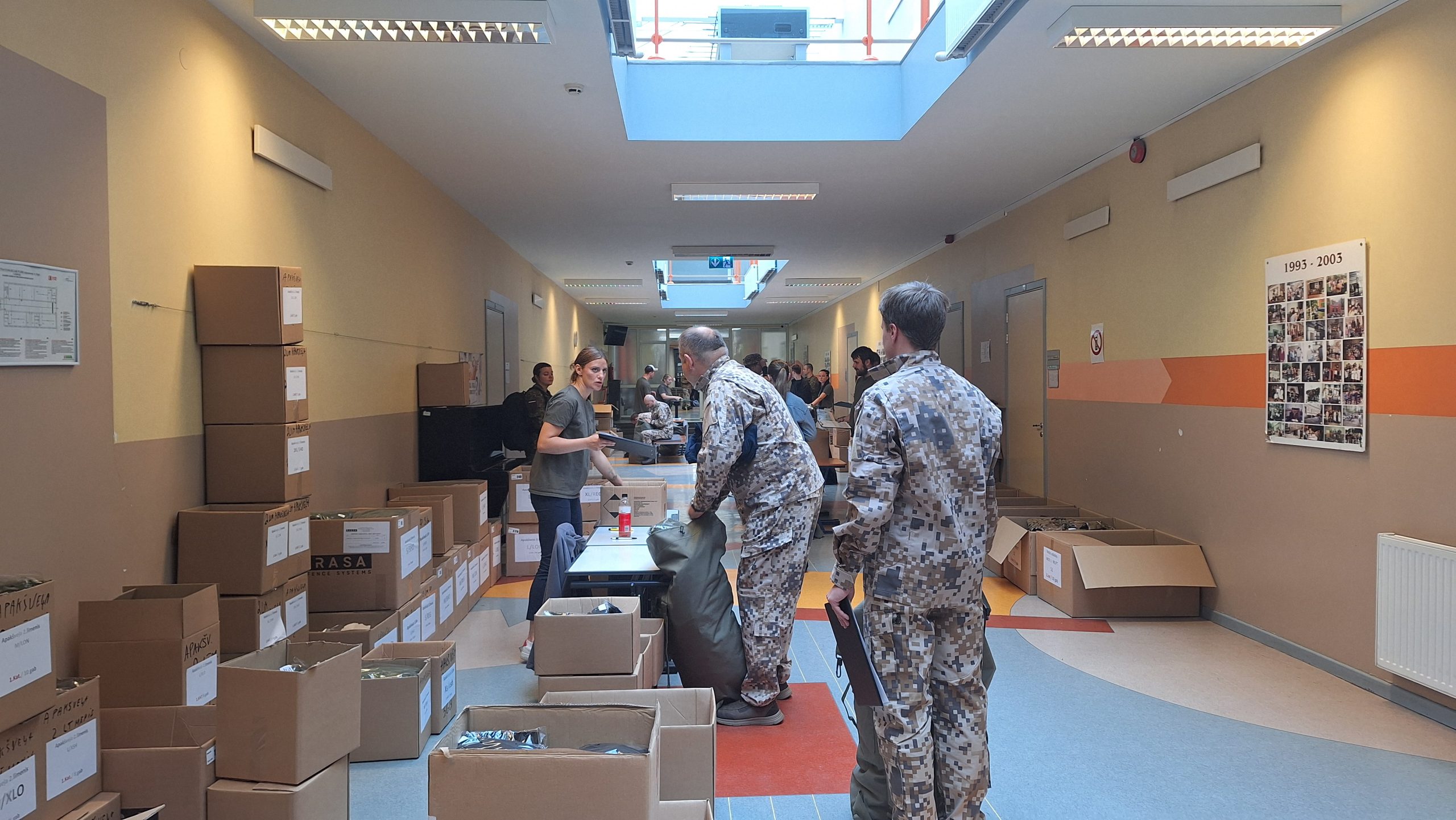 Plašs koridors skolā, kur militārpersonas un brīvprātīgie kārto militāro ekipējumu