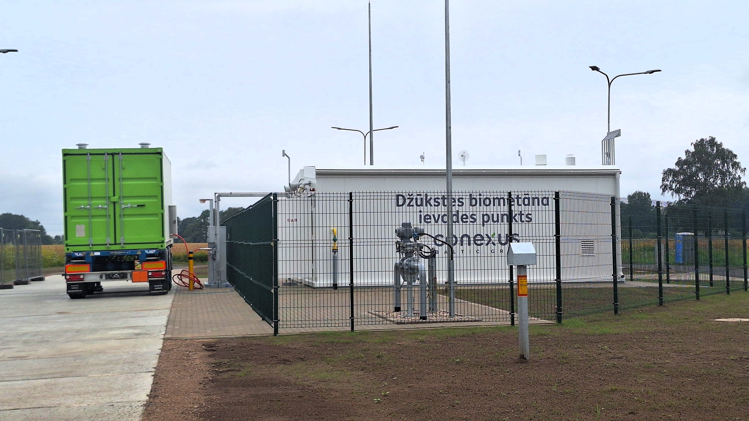 Latvijā pirmais publiskais biometāna ievades punkts Džūkstē ar zaļu kravas konteineru blakus.