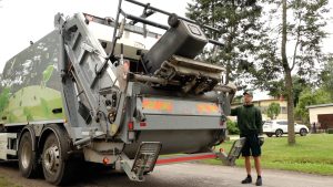 ZAAO elektriskais atkritumu vedējs, kas paceļ atkritumu konteineru, blakus stāv darbinieks.