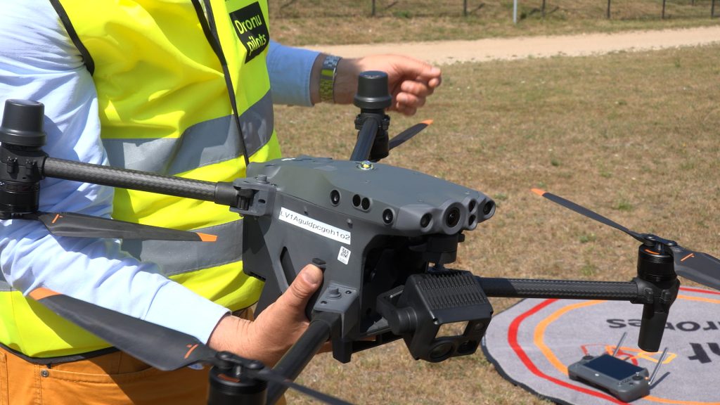 Persona vestē, turot rokās DJI Matrice 30T dronu ar termokameru un lāzera tālmēru, kas sagatavots lidojumam