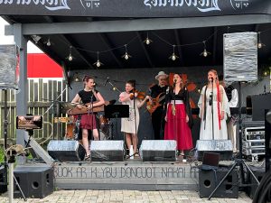 Etnodžeza ansamblis “Bruoļi i muosys” uzstājas uz skatuves, muzicējot ar kokli, vijoli, basģitāru, taustiņinstrumentiem un dziedot