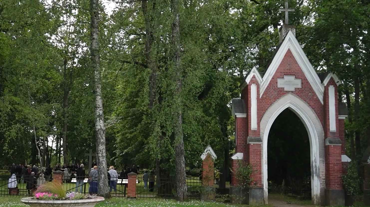 Cilvēki pie ieejas Cēsu Vācu kapos, pie sarkanu ķieģeļu vārtiem
