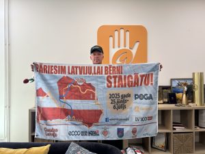 Raimonds Požarskis tur plakātu ar uzrakstu “Pāriesim Latviju, lai bērni staigātu!” labdarības gājienam.