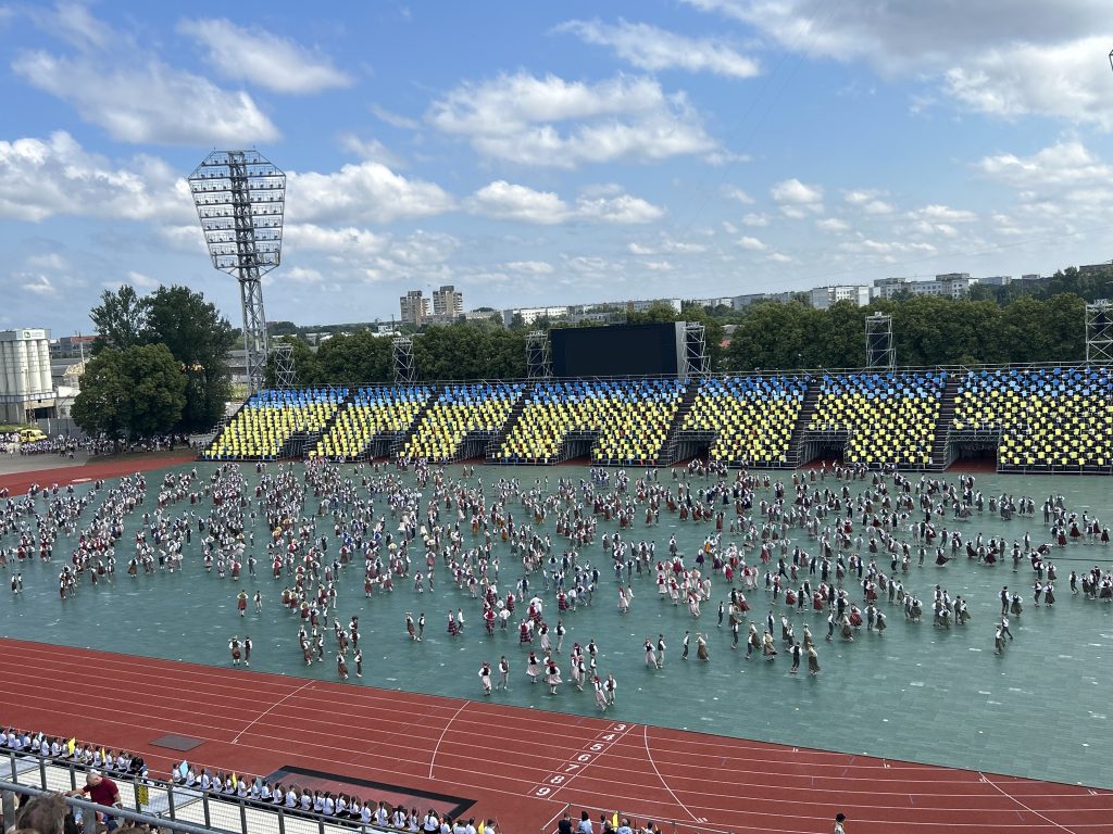 Daugavas stadions ar dejotājiem tradicionālos tērpos, kas izkārtojušies dejā uz laukuma.