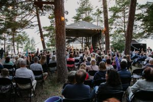 Publika sēž pie koku ieskautas āra skatuves kamermūzikas festivāla "Satikšanās Saulkrastos" noslēguma koncertā Baltajā kāpā
