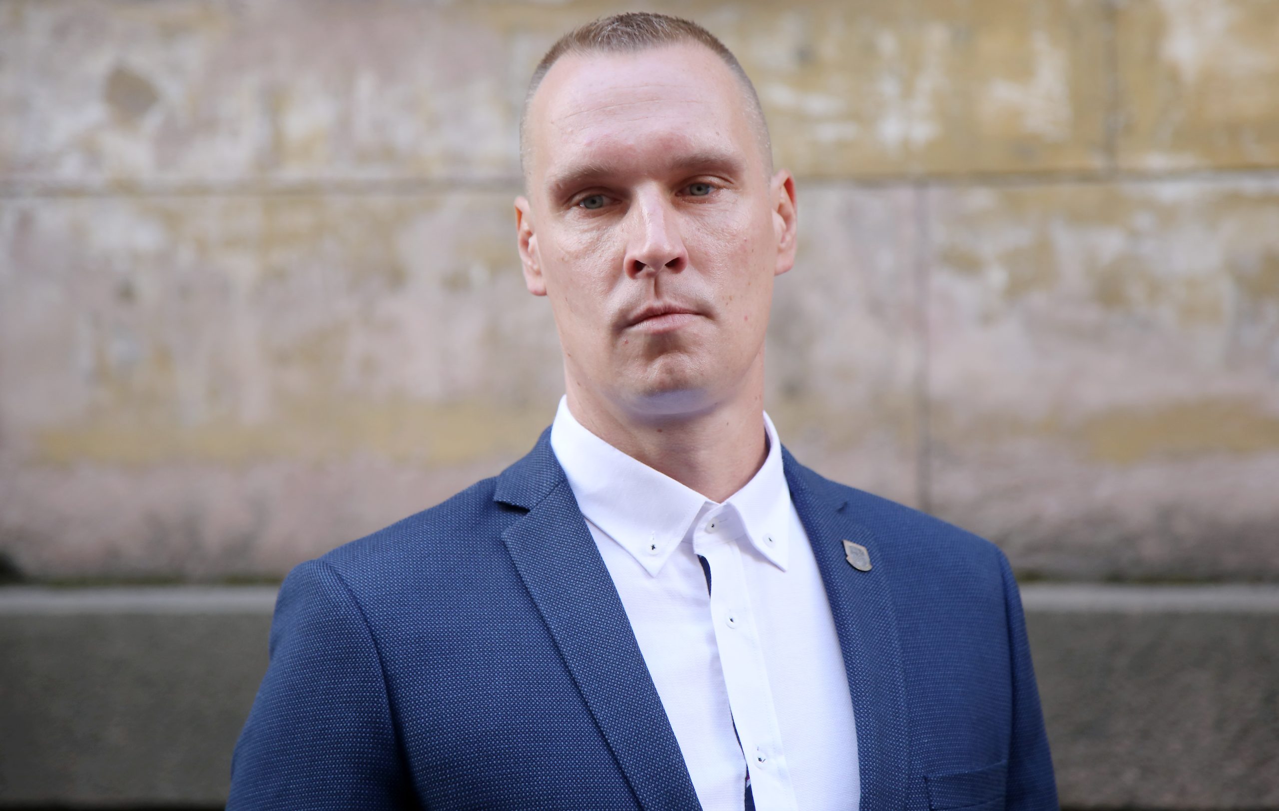 Andris Vurčs - jauns vīrietis ar īsiem matiem, stāv uz neitrāla fona, ģērbies uzvalkā