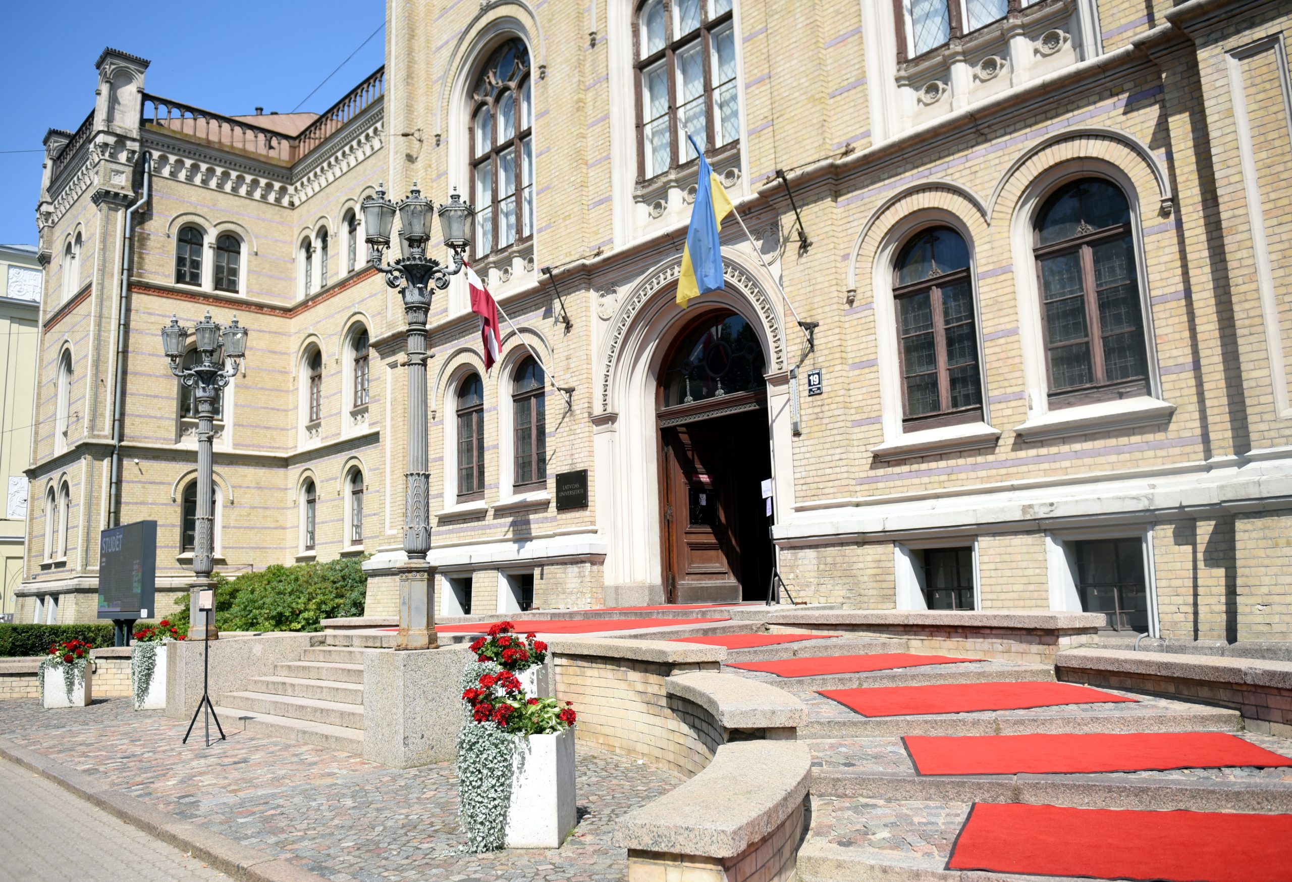 Latvijas Universitātes galvenā ēka ar sarkanajiem paklājiem pie ieejas.