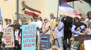 Pāvilostas iedzīvotāju protests pret vēja parku būvniecību ar plakātiem un Latvijas karogiem.