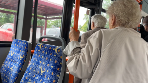 Gados vecāka sieviete turas pie autobusa stieņa, kamēr stāv autobusā