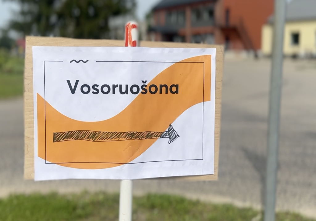 Zīme ar oranžu apli, melnu bultu un uzrakstu "Vosoruošona"