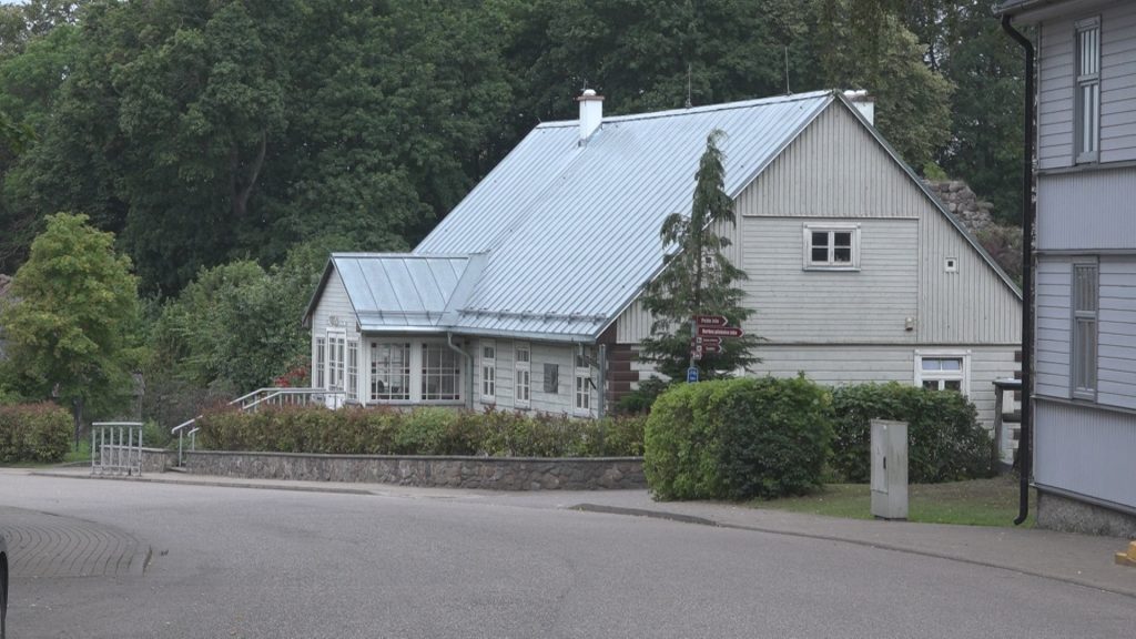 Veclaikīga, gaiši pelēka koka māja ar metāla jumtu un apstādījumiem