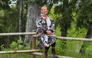 Vineta Zālīte sēž uz koka žoga lauku ainavā