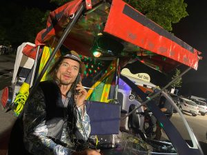 Velotaksometra vadītājs ar cepuri un mikrofonu naktī festivālā
