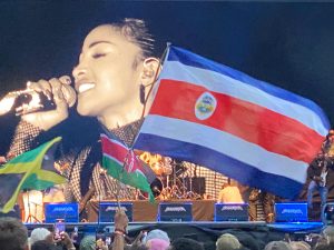 Dziedātāja uz skatuves Summerjam festivālā ar dažādu valstu karogiem priekšplānā